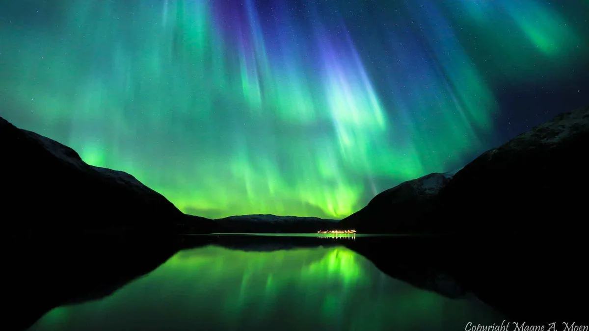 Small group beside a Mercedes minibus watching the aurora arc over a frozen lake on a Tromso Northern Lights tour, northern Norway