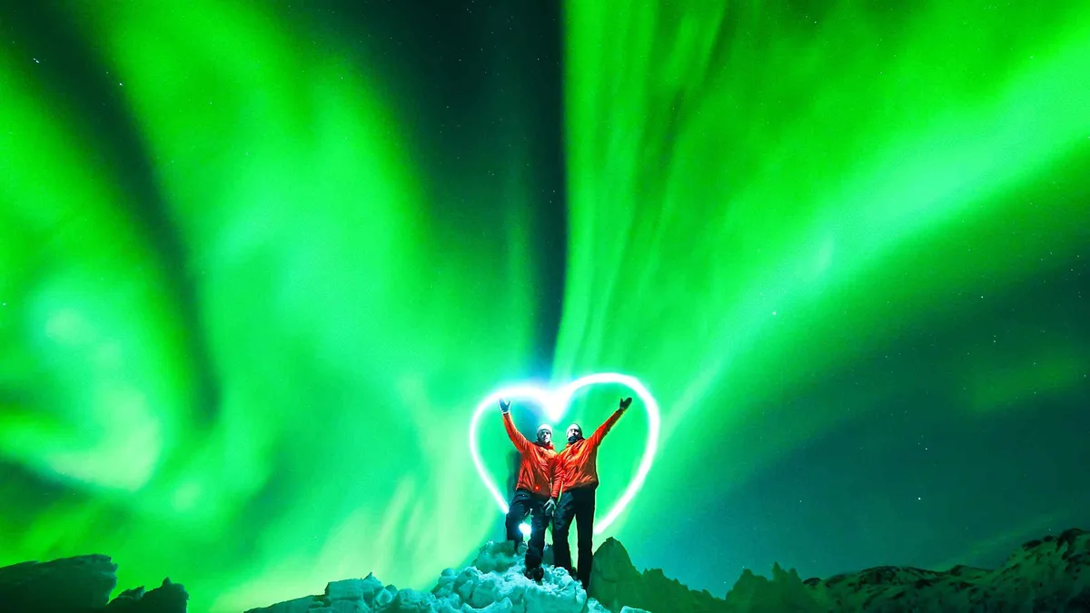 Guide in an orange jacket photographing guests under the aurora on a Tromso Northern Lights tour run by Arctic Breeze, Troms county